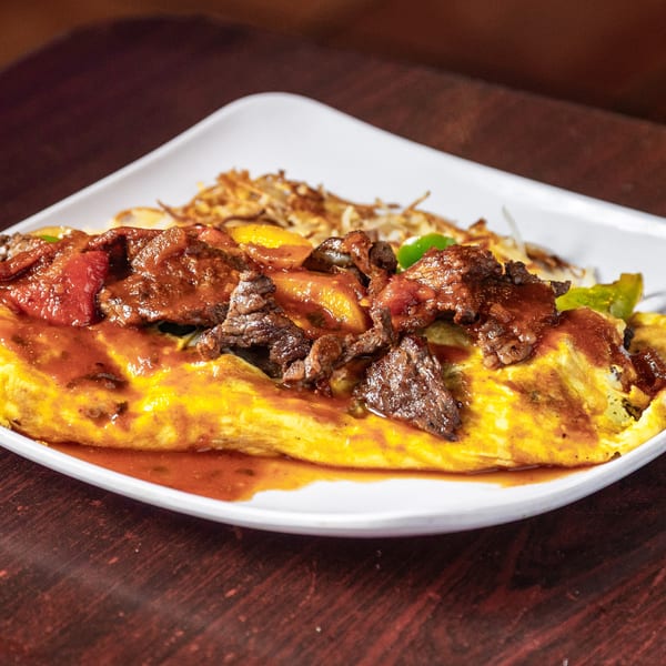 A Mexican omelet with steak, peppers, and sauce, served with hash browns on a white plate.