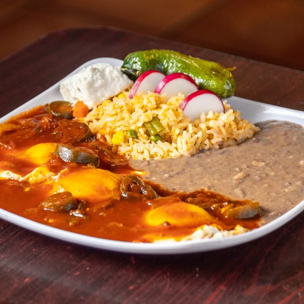 A Mexican breakfast plate with huevos rancheros, rice, refried beans, radishes, and a green chili.