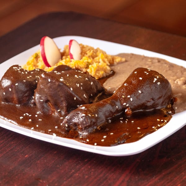 Los Molcajetes' chicken mole with sesame seeds, rice, refried beans, and radish slices.