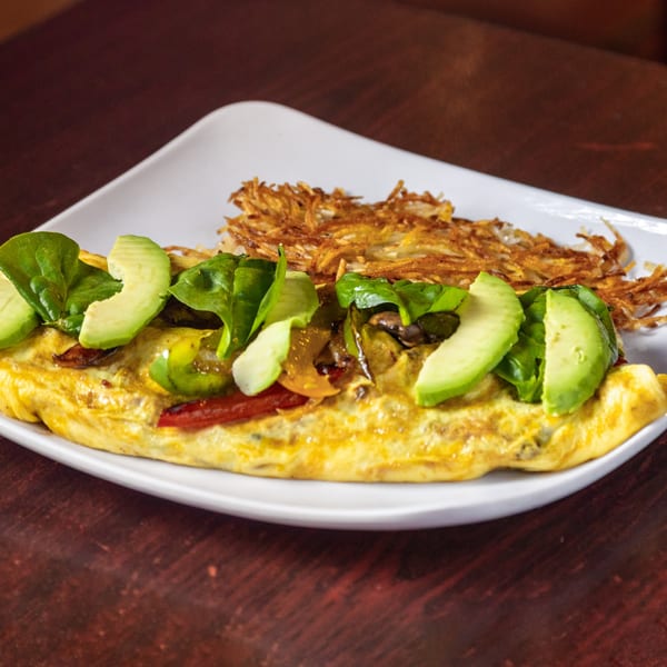 A Los Molcajetes omelet with avocado, spinach, and hash browns on a white plate.