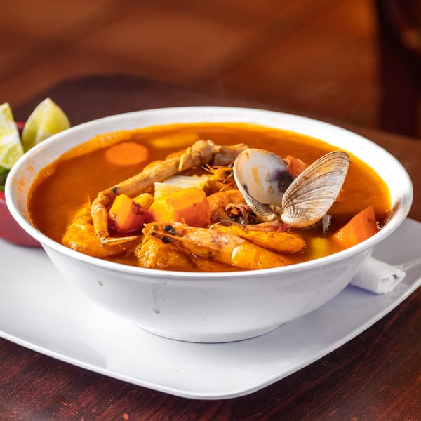 A vibrant Mexican seafood soup, Los Molcajetes' Caldo de Mariscos, with shrimp, crab, clams, and vegetables.