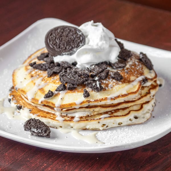 Stack of pancakes topped with whipped cream, crushed Oreos, and a whole Oreo cookie.