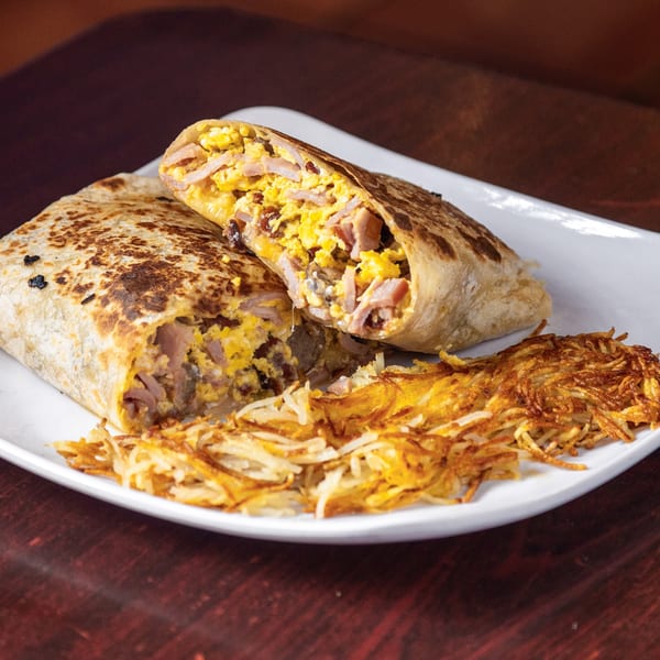 A breakfast burrito, cut in half to show scrambled eggs, bacon, and cheese, served with hash browns.