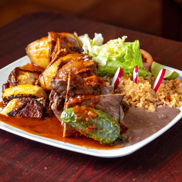 Mexican dish with sauced meat, rice, refried beans, grilled potatoes, and a side salad with radishes.